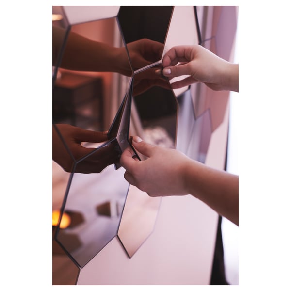 Person arranging multi-panel mirror on wall. Hands manipulate reflective panels, showcasing versatility in hanging options.