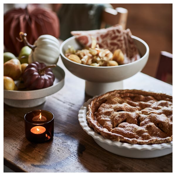 Cosy autumn scene: lit candle, apple pie in dish, fruit bowl with pumpkins.