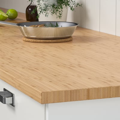 A wooden kitchen counter with a frying pan, plant, and limes. The bamboo worktop is durable and resistant to everyday kitchen use.