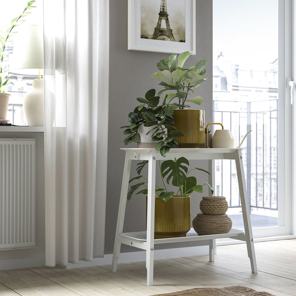 White plant stand near window with decorative items and greenery.