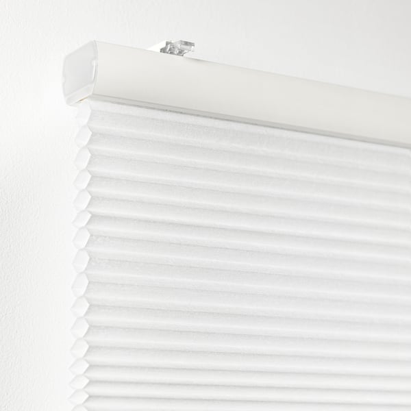 White cellular blind installed against a white wall, partially rolled down for light control, with a visible pull cord slot and brackets.