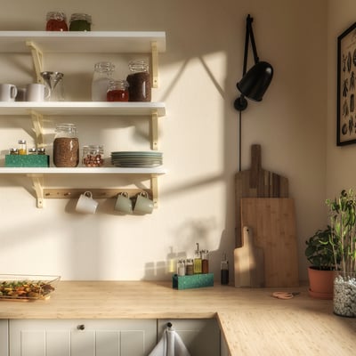 Kitchen counter with wooden countertop, white cabinet, shelves with jars, mugs, cutting boards, and green plants.