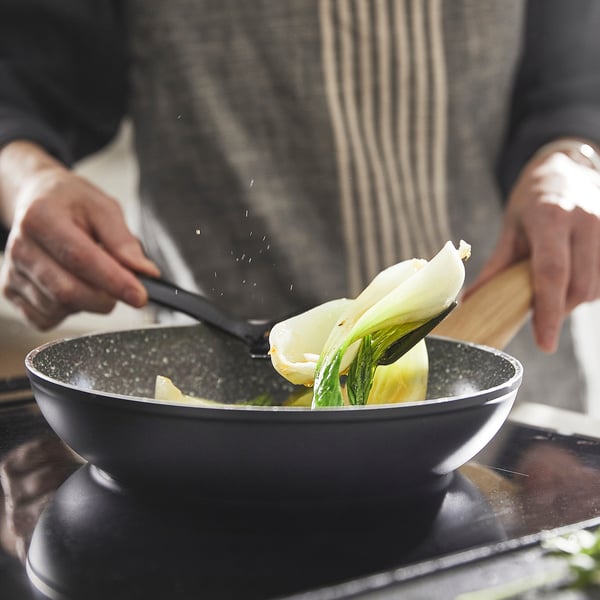 Person cooks cabbage in non-stick pan. The pan has thick base for even heat, and comfortable handles for easy lifting.