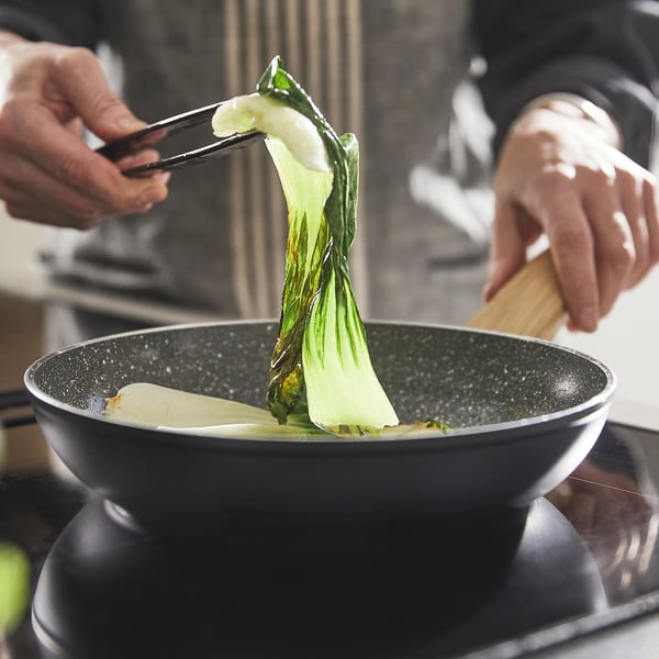 Person cooking vegetables in a non-stick frying pan, using wooden utensils.