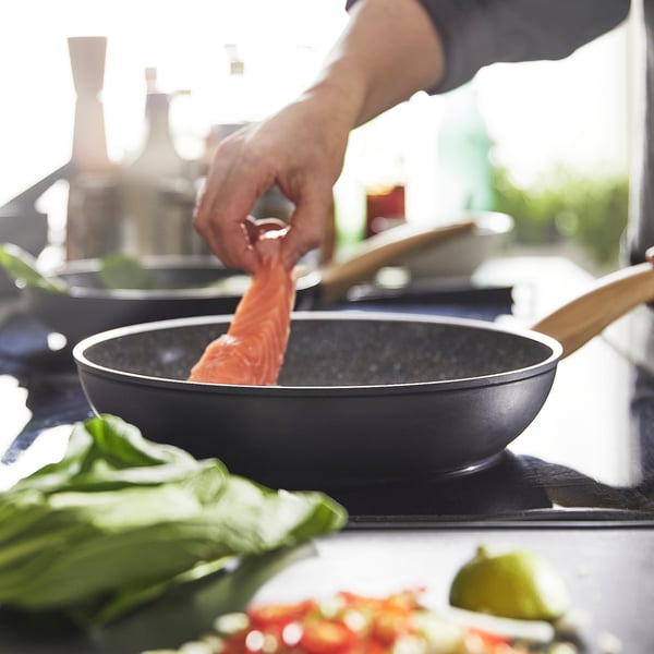 A person is cooking fish in a non-stick frying pan with a wooden handle, demonstrating its ease of use and even heat distribution.