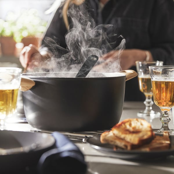 Pan on table with steam, food, and drinks. Wooden handles for easy lifting.