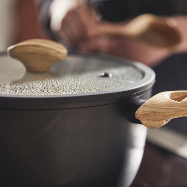 Black saucepan with wooden handle on stove, steam vent visible, sol-gel ceramic non-stick coating.