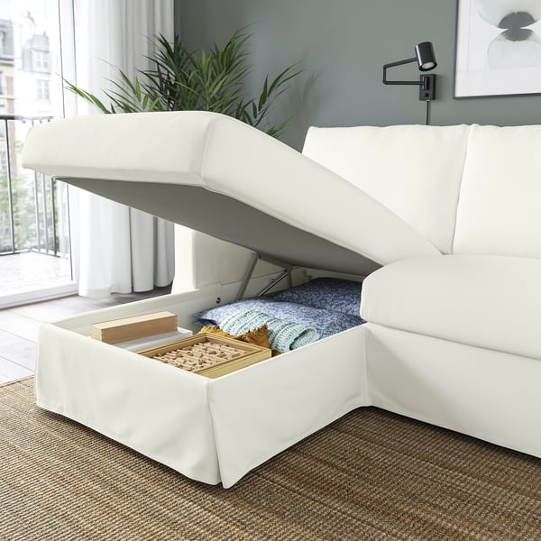 Modern white sofa with open storage chaise, revealing blankets and game, ideal for family use.