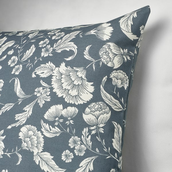 Square throw pillow with blue background and intricate white floral design.