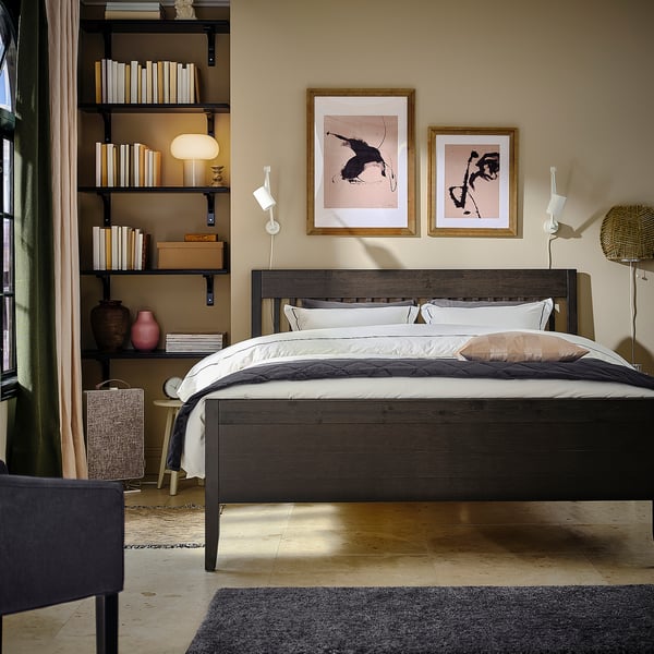 Modern bedroom IDANÄS wooden bed with white linens, abstract wall art, and black shelves filled with books.