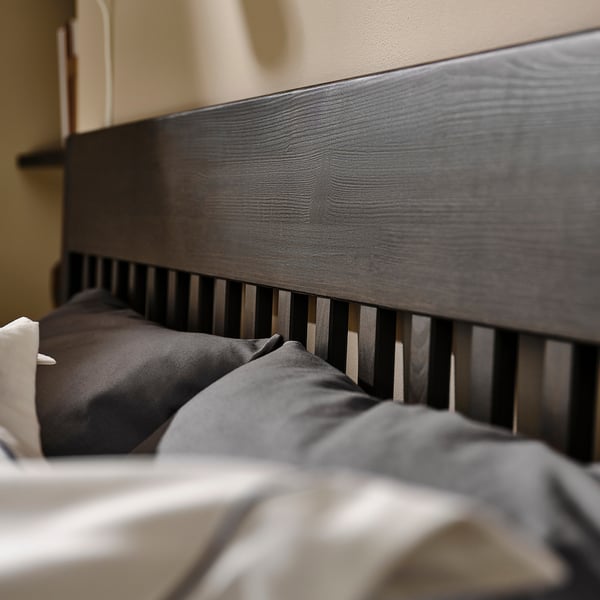 Modern dark wood bed with grey bedding and metal slats.