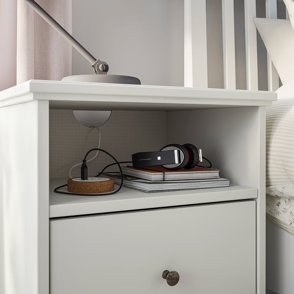 White IDANÄS bedside table with shelves, headphones, books, lamp.