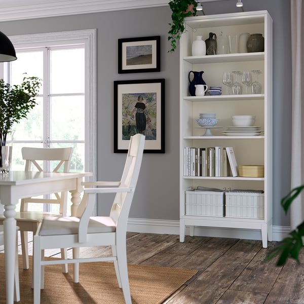 White bookcase, grey wall, framed art, dining chair, window, dishes, vases.
