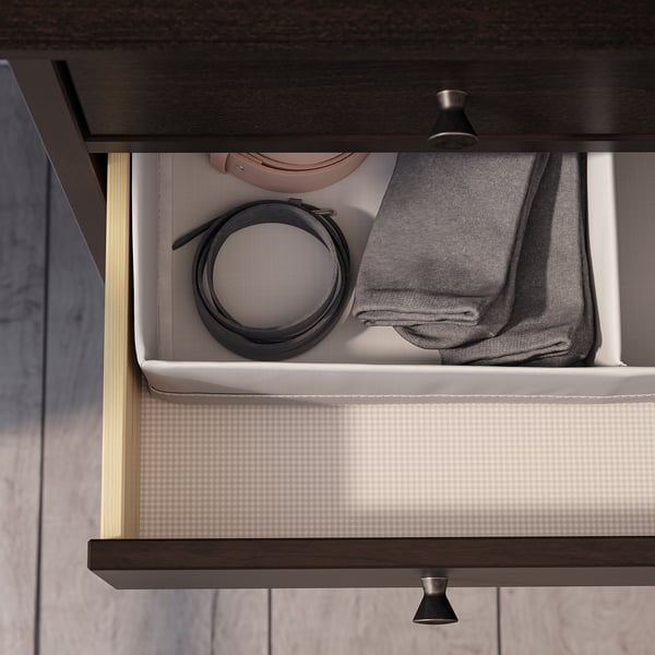 Open wooden drawer with metal handle, containing rolled black belt and grey clothes.