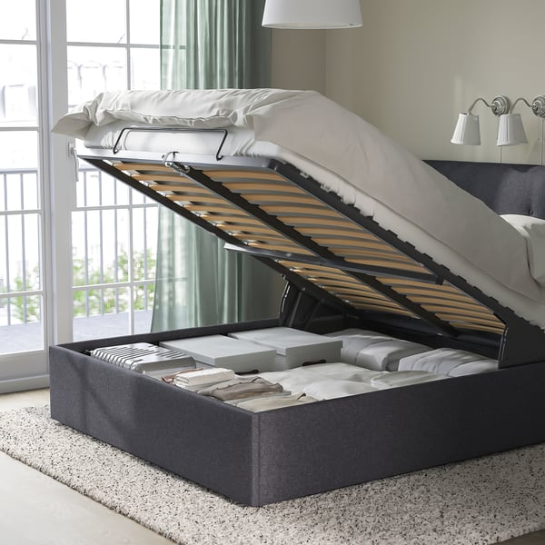 Upholstered bed with lift-up base for storage. Headboard slants for comfort, storage space visible under bed.
