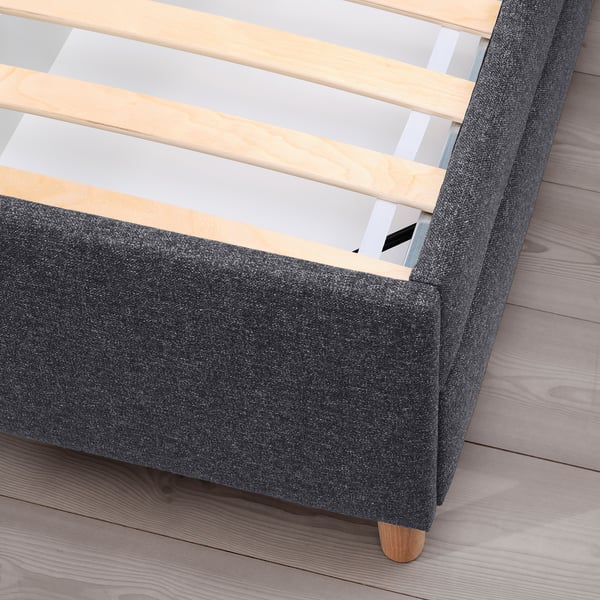 Dark grey upholstered bed with wooden slats and legs, showcasing storage drawers.