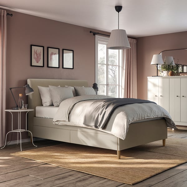 Modern bedroom with IDANÄS beige bed, hanging lamps, white drawers, and large rug. Bed is centred, drawers right, rug below.