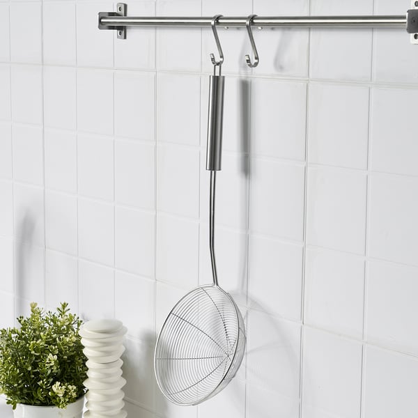 Silver skimmer hangs on wall hook near stove, ready to remove items from pots.