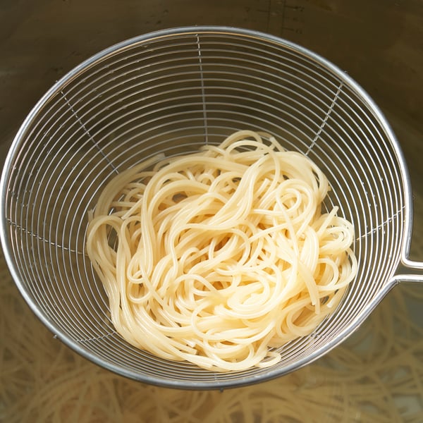 Stainless steel skimmer filled with cooked noodles, ideal for straining.