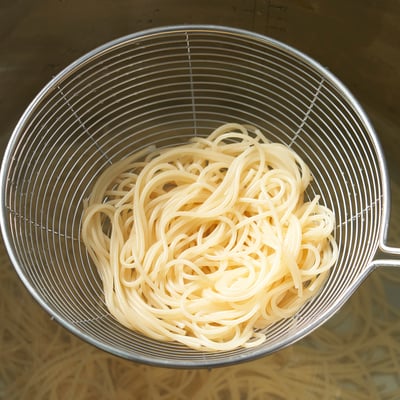 Stainless steel skimmer filled with cooked noodles, ideal for straining.