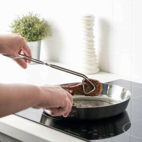 Hands using tongs to flip steak in a pan, demonstrating kitchen utensils grip and cooking assistance.