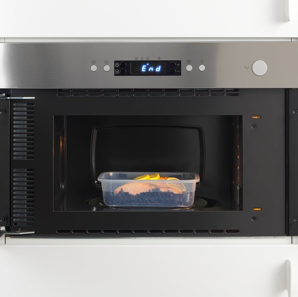 Stainless steel microwave with digital display heating plastic food container, showing reheating function.