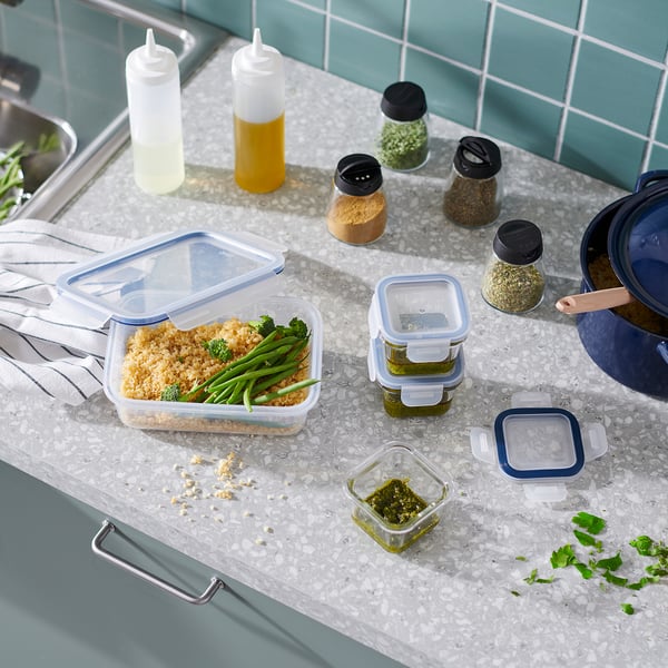 Kitchen counter with various food containers, bottles, and a pan; IKEA 365+ containers in blue, square shape.