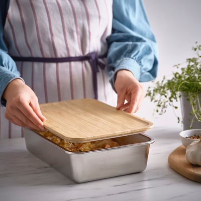 Person placing bamboo lid on stainless steel food container on countertop, covering dish.