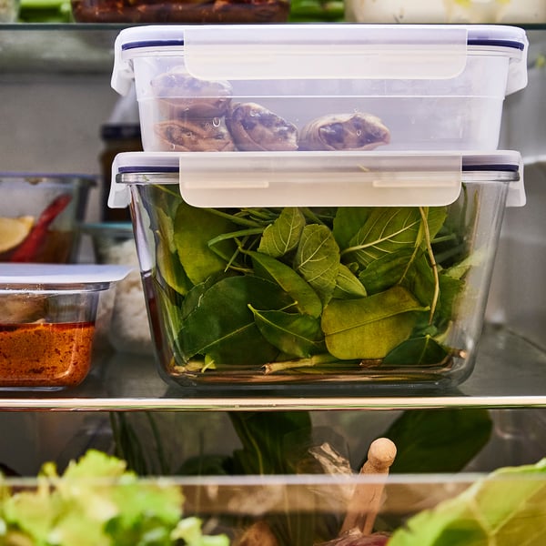Clear glass container with snap-lock lid, filled with green leafy vegetables. Stored in a refrigerator.