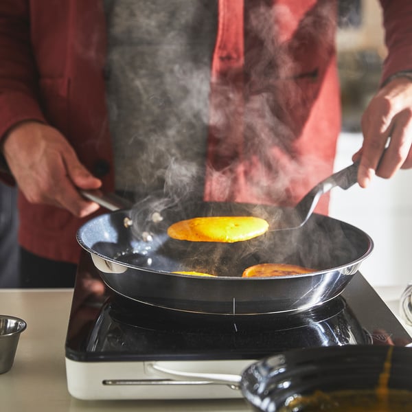 Person cooking in pan with steam rising, likely using IKEA 365+ non-stick pan on an electric stove.