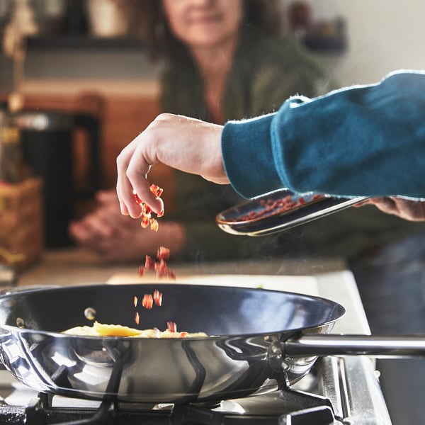Cooking with frying pan on stove, adding food.