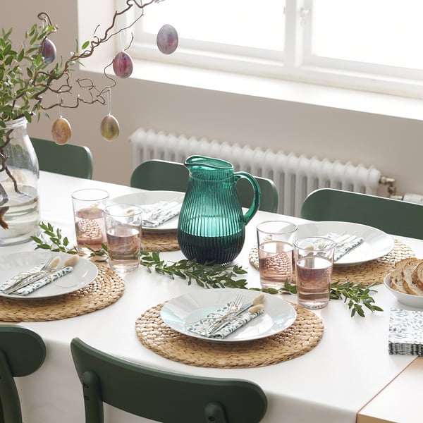 A dining table set with IKEA 365+ glasses, green pitcher, plates, cutlery, and napkins, ready for a meal.