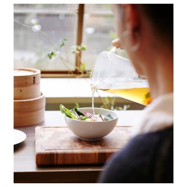 Pouring yellow liquid over salad in white bowl near bamboo steamer.