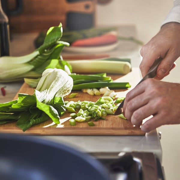 Hand chops green onions on wooden cutting board with knife.