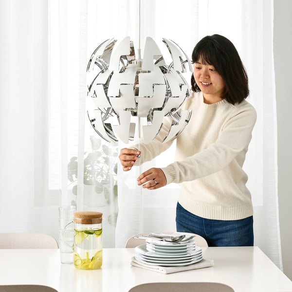 A person adjusts an IKEA PS 2014 pendant lamp, changing its shape and light intensity by pulling strings, casting patterns on the ceiling.