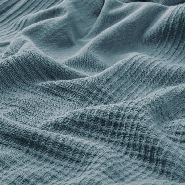 Close-up of soft, textured blue cotton bedspread, showcasing its weave and warmth.