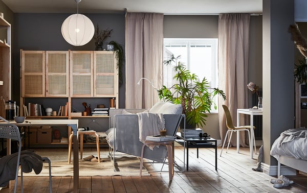 Modern living room with IVAR wooden shelves, grey walls, hanging light, beige curtains, plants, and minimalist furniture.