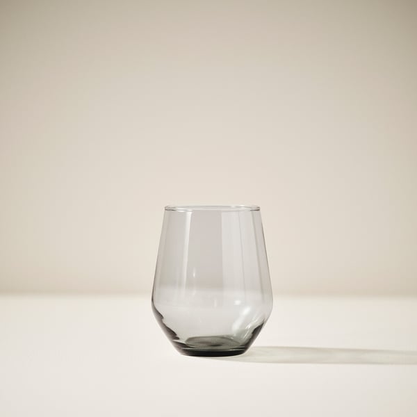 Single clear glass with wide, round bowl sits on plain light surface, reflecting subtle shadows.