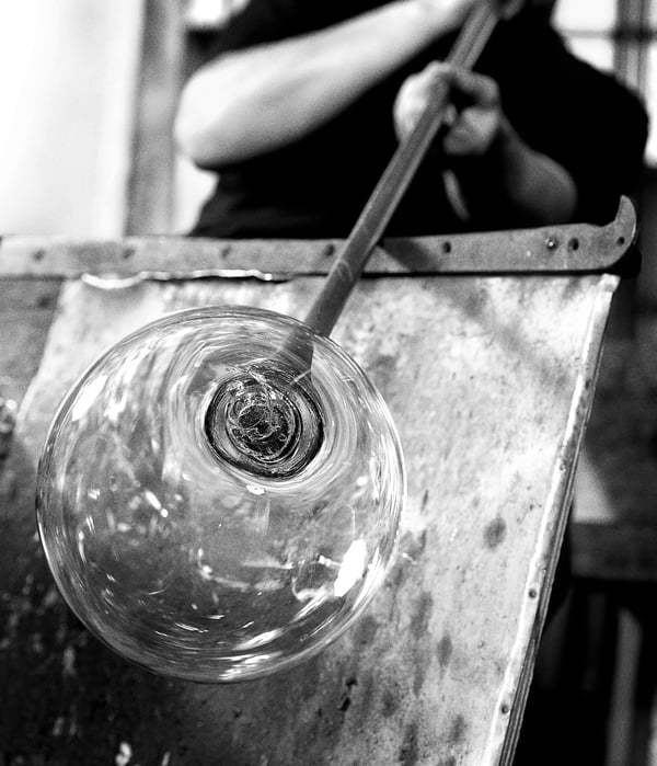Black and white a person mouthblowing glass into a round shape, creating a unique lamp shade.