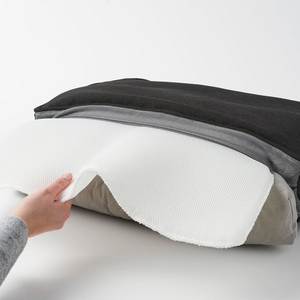 Hand peeling off cover of black and white JÄRPÖN/DUVHOLMEN outdoor cushion. Zipper visible, showing easy removal for cleaning.
