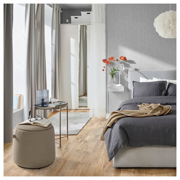 Modern bedroom featuring JÄRRESTAD grey pouffe, dark bedding, red flowers, and minimalist decor.