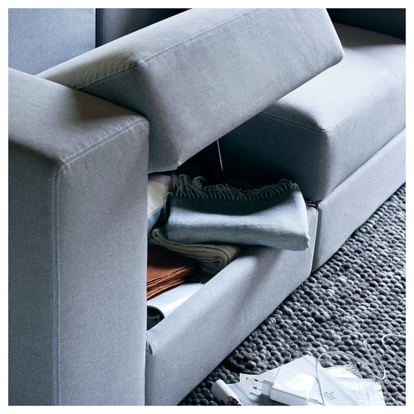 Modern grey modular sofa with folded blankets and charging station on knitted rug.