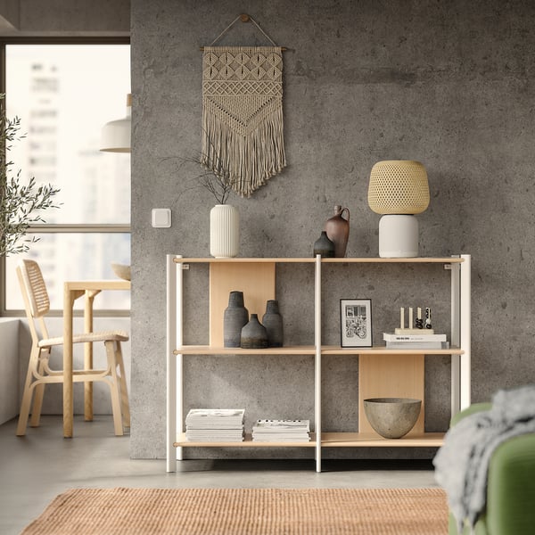 Modern living room: grey JÄTTESTA shelf with vases, books, and green rug. Concrete wall, macrame, and wooden chairs.