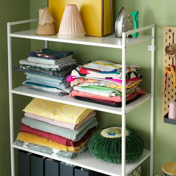 White metal shelving unit with colourful fabric stacks and decorative items.