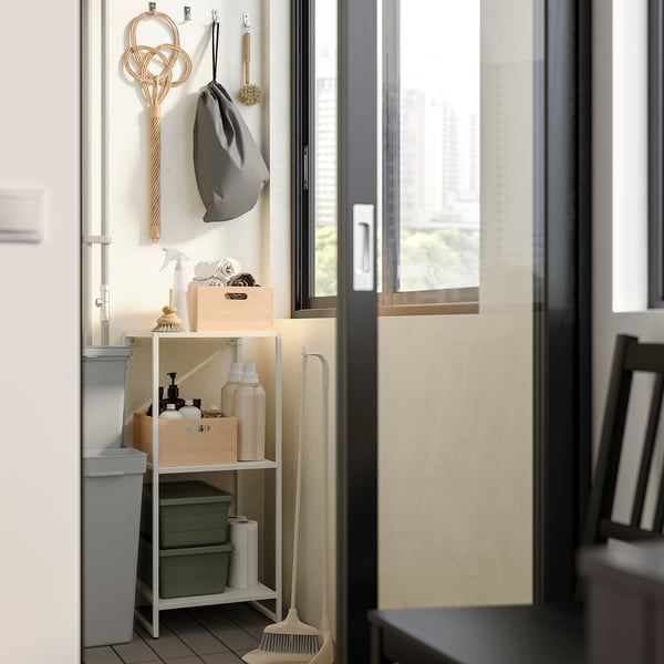 Small bathroom storage rack with shelves holding cleaning supplies, beside a window with a mop and hooks for accessories, everything organised neatly.