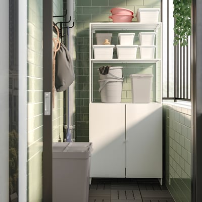 Small white JOSTEIN storage shelf, green tile wall backdrop, plastic bins on shelves, hanging bag, indoor/outdoor use.