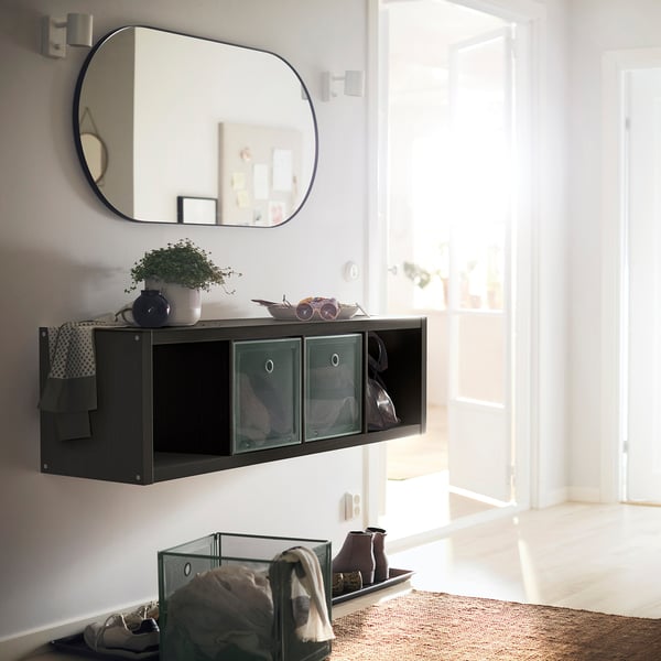 Modern entryway with black KALLAX shelving unit, mirror, and decor on top, baskets below, near white door.