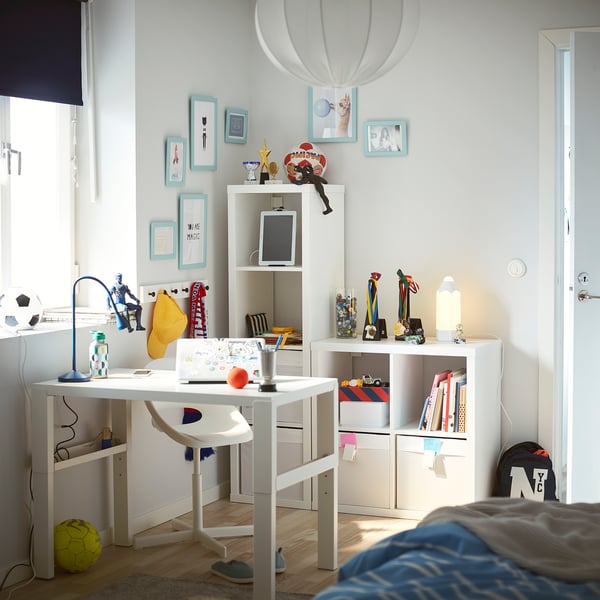 Bright kids room with white KALLAX shelving, colourful decor, and sports items. A desk, chair, and personal mementos on the wall.