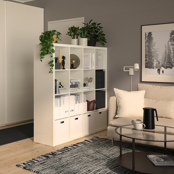 Modern living room with KALLAX white shelving unit, decor, plants, beige couch, coffee table, and black picture frame.