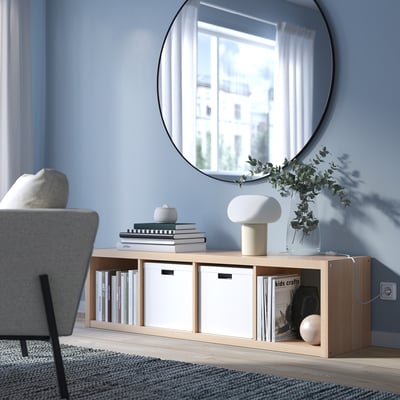 KALLAX shelf against blue wall with books, lamp, and large mirror reflecting window and building.